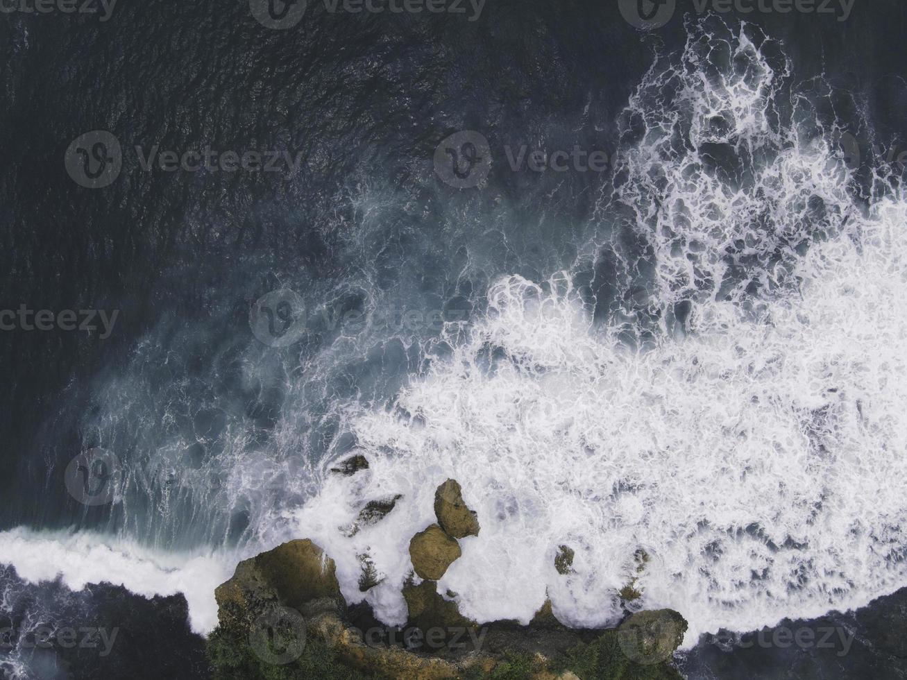 vista aerea dall'alto verso il basso delle onde oceaniche giganti che si infrangono e si schiumeggiano nella spiaggia di corallo foto