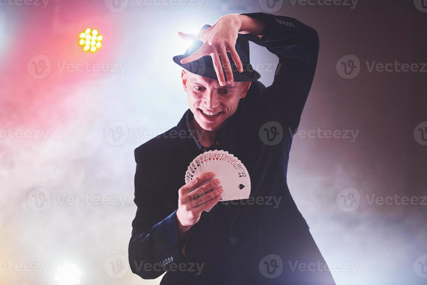 mago che mostra trucco con le carte da gioco. magia o destrezza, circo, gioco d'azzardo. prestigiatore in camera oscura con nebbia foto