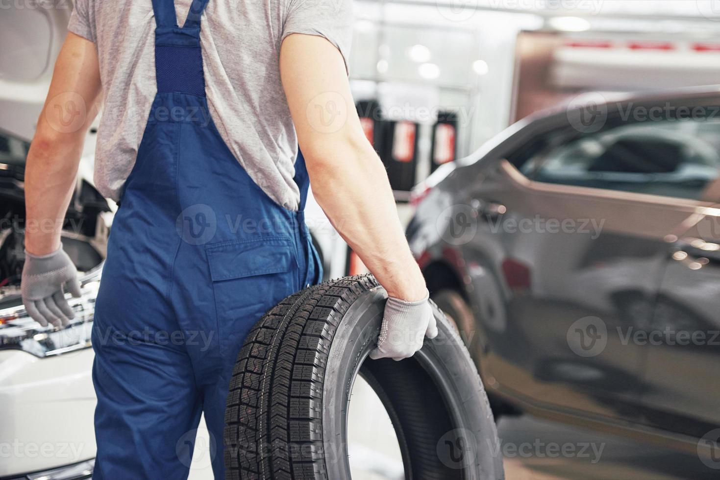 meccanico che tiene un pneumatico al garage di riparazione. sostituzione gomme invernali ed estive foto