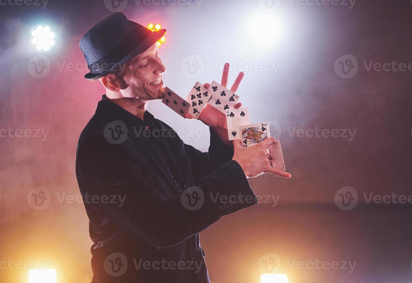 mago che mostra trucco con le carte da gioco. magia o destrezza, circo, gioco d'azzardo. prestigiatore in camera oscura con nebbia foto