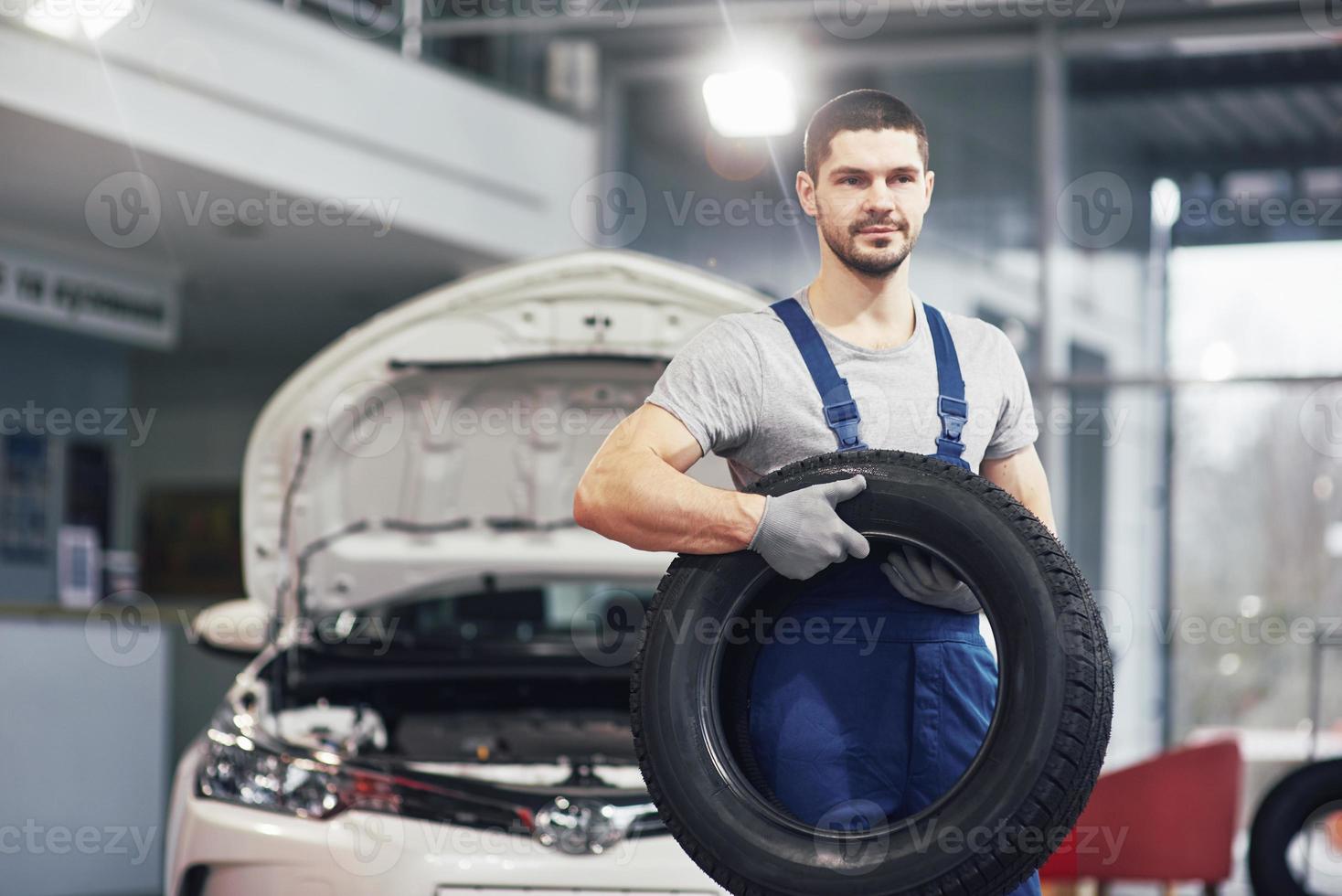 meccanico che tiene un pneumatico al garage di riparazione. sostituzione gomme invernali ed estive foto