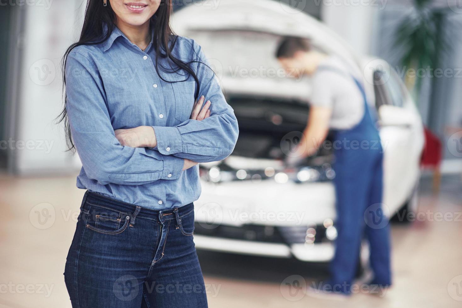 donna in un garage per auto che riceve un servizio meccanico. il meccanico lavora sotto il cofano dell'auto foto