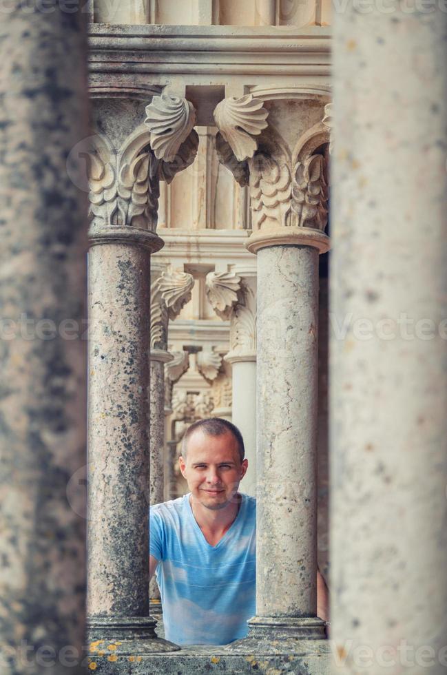 giovane viaggiatore che guarda l'obbiettivo e posa tra le colonne di pietra del castello medievale di leiria in portogallo foto