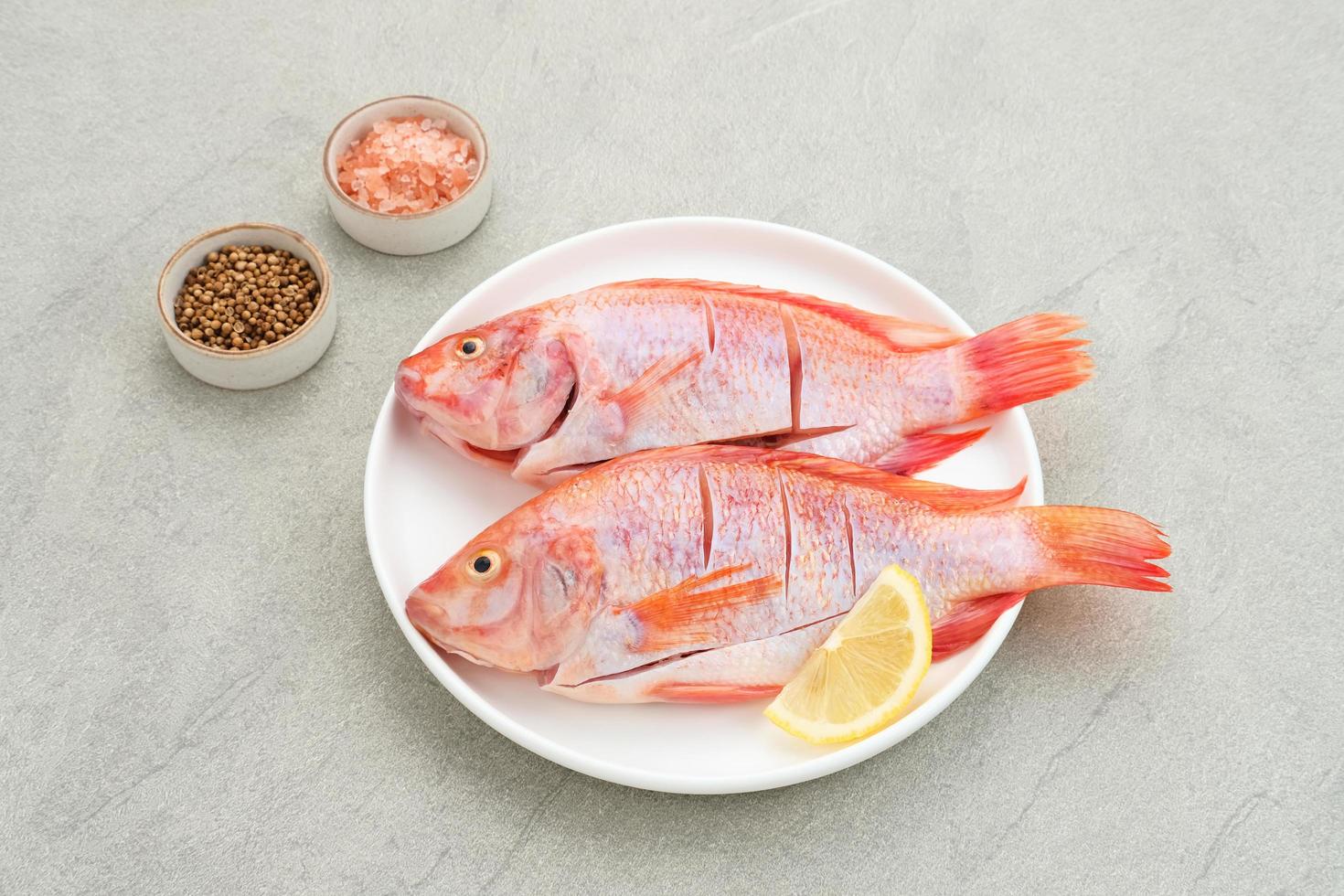 il pesce crudo di tilapia rossa è una specie di pesce d'acqua dolce, servito su un piatto bianco con spezie e limone. messa a fuoco selezionata foto