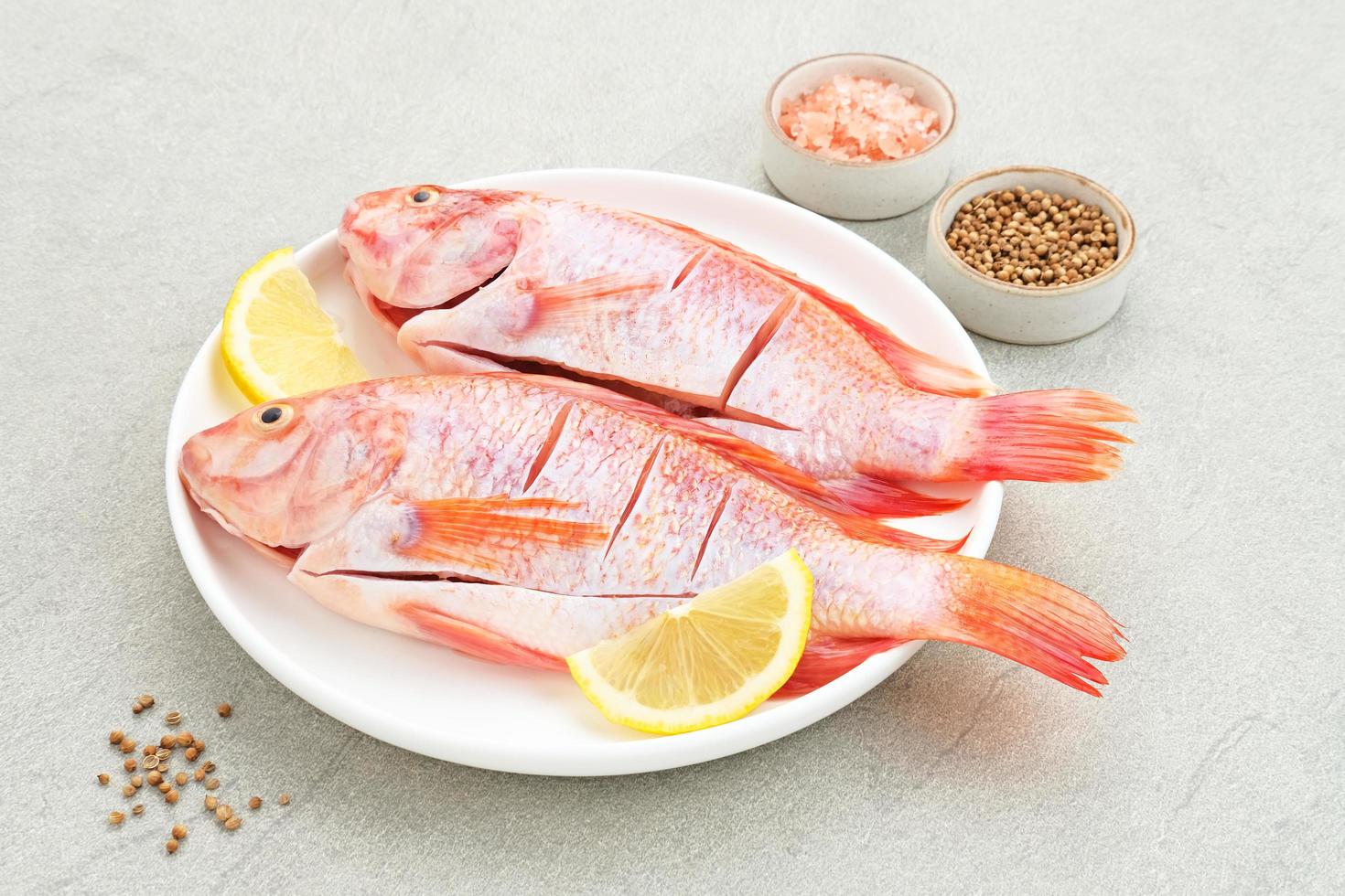 il pesce crudo di tilapia rossa è una specie di pesce d'acqua dolce, servito su un piatto bianco con spezie e limone. messa a fuoco selezionata foto