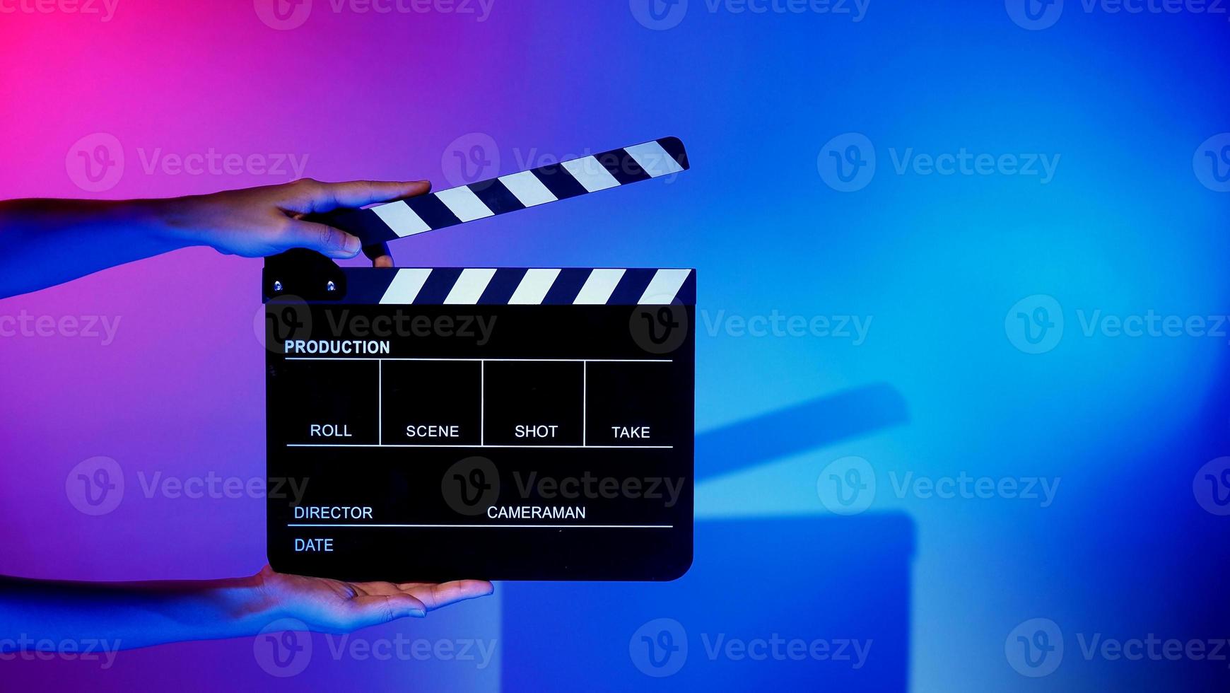 la mano tiene il ciak vuoto per la produzione di film su sfondo colorato in studio foto