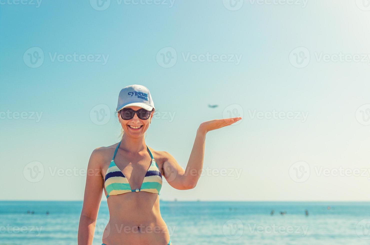 giovane bella ragazza in bikini, occhiali da sole e berretto sulla spiaggia in posa di larnaca foto