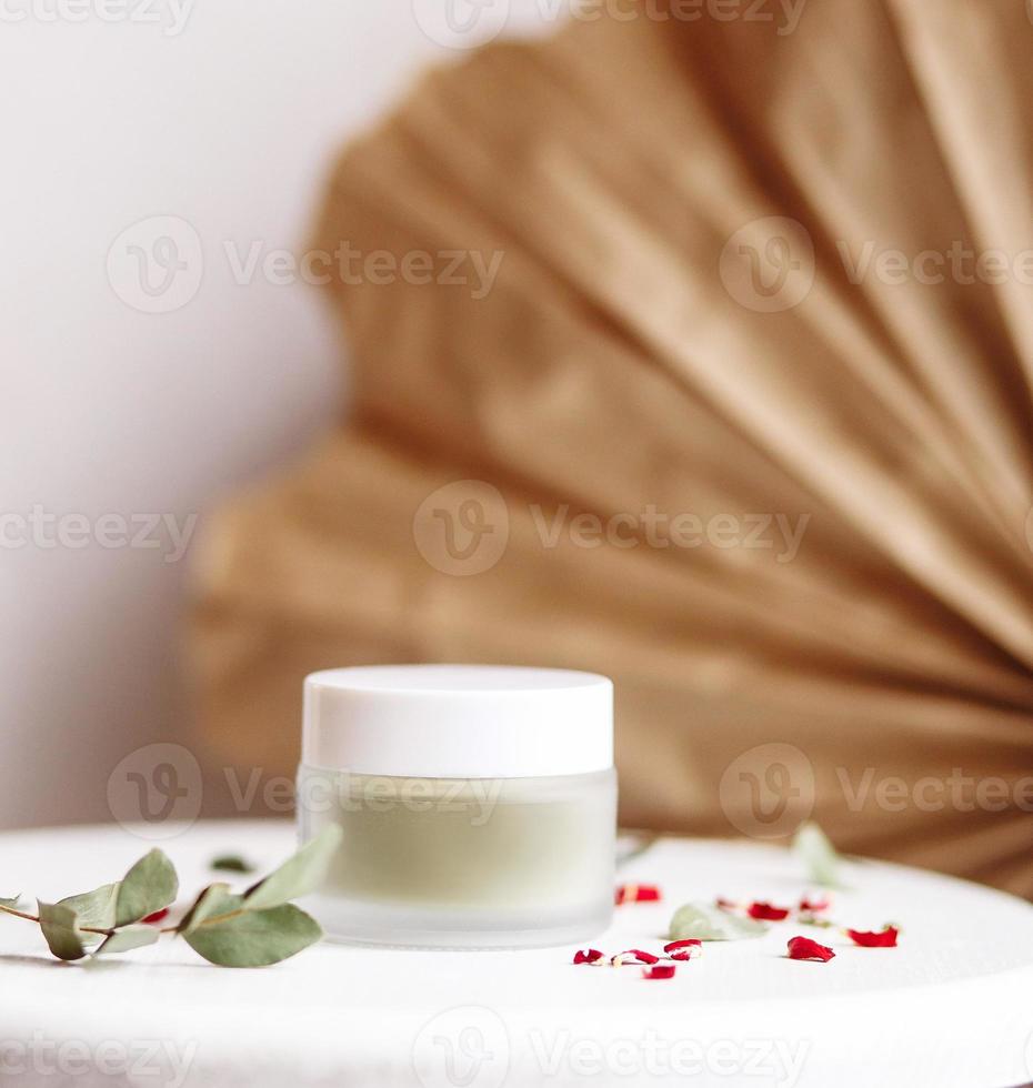 maschera cosmetica in polvere. vasetto di vetro con matcha su fondo bianco con petali secchi. foto