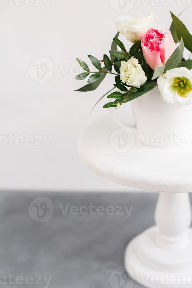 bouquet primaverile in vaso bianco su supporto bianco in legno. rose, tulipani e lisianthus. foto