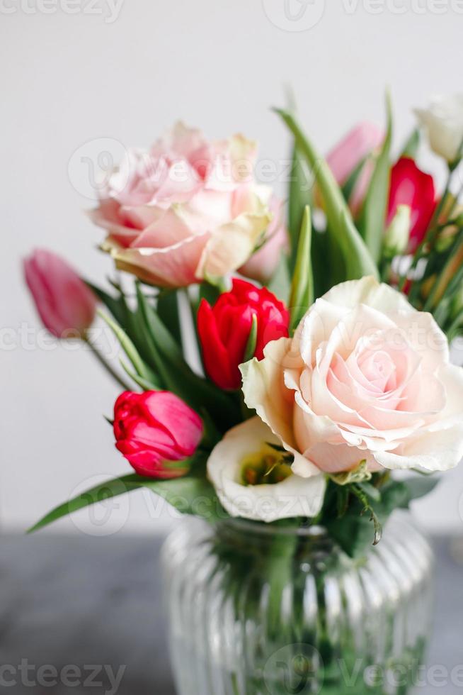 bouquet primaverile in vaso di vetro trasparente. rose, tulipani e lisianthus. foto