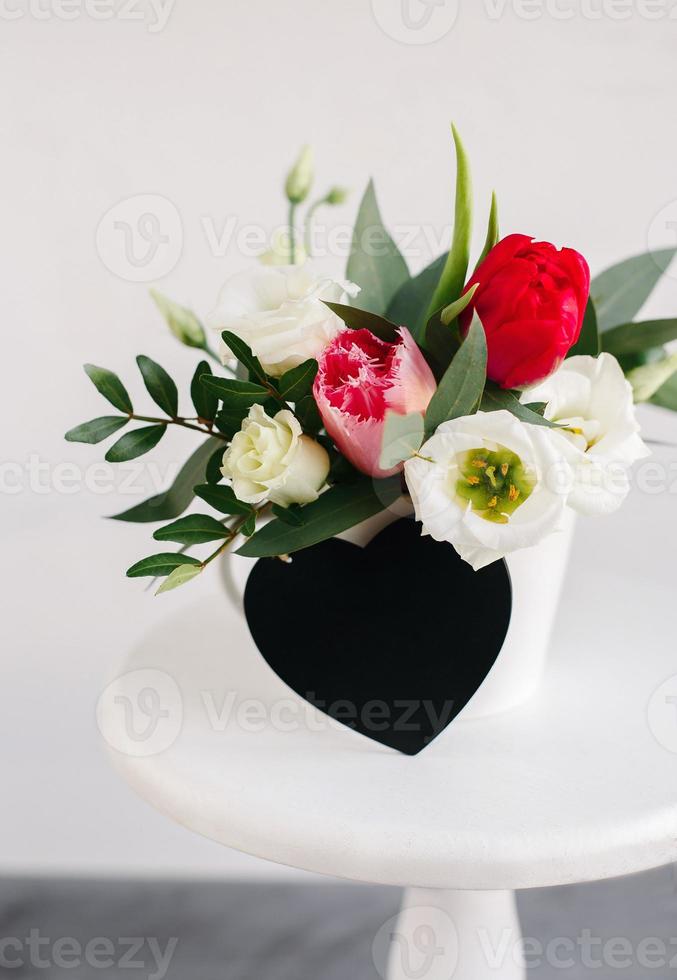 copyspace cuore bordo nero. bouquet primaverile in vaso bianco su supporto bianco in legno. rose, tulipani e lisianthus. foto