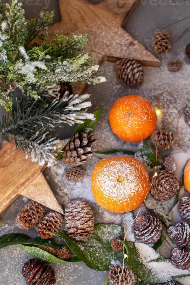mandarini arancioni su sfondo grigio nell'arredamento di Capodanno con pigne marroni e foglie verdi. decorazione natalizia con mandarini. deliziosa clementina dolce. foto