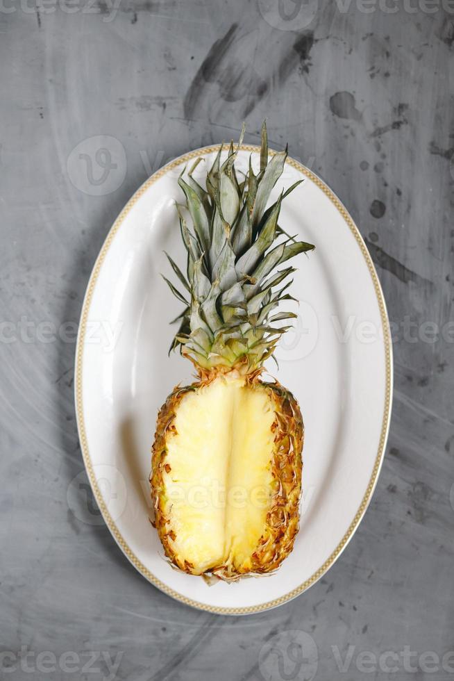 piatto bianco con ananas maturo affettato su sfondo grigio cemento. foto