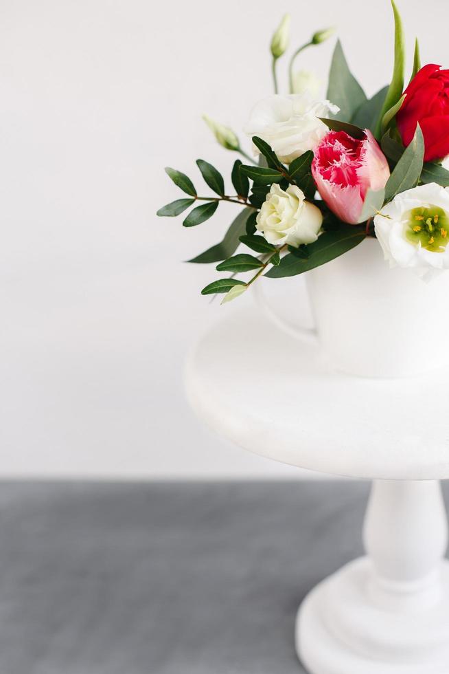 bouquet primaverile in vaso bianco su supporto bianco in legno. rose, tulipani e lisianthus. foto