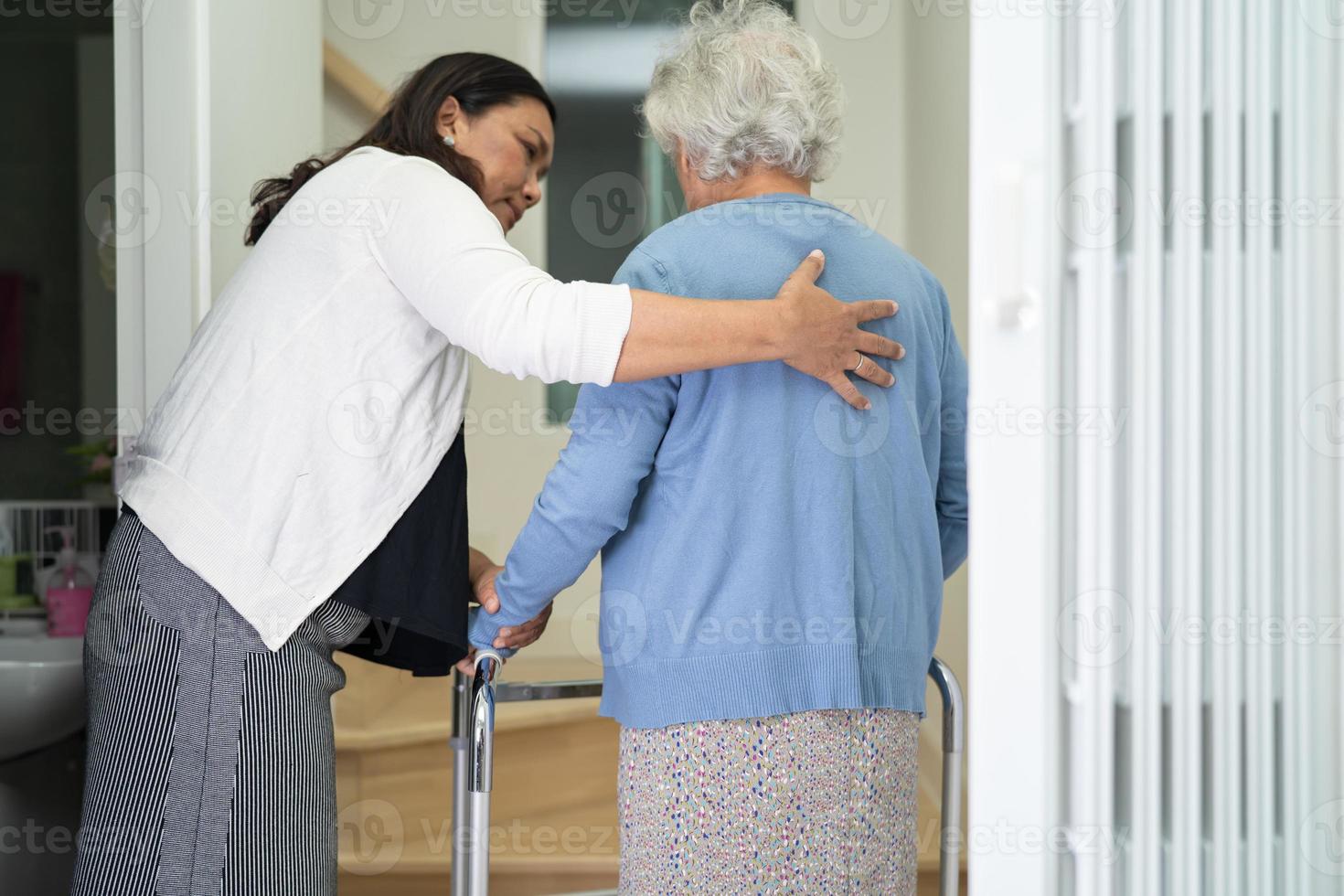 il caregiver aiuta la donna anziana asiatica o anziana a camminare con il supporto del deambulatore su per le scale di casa. foto