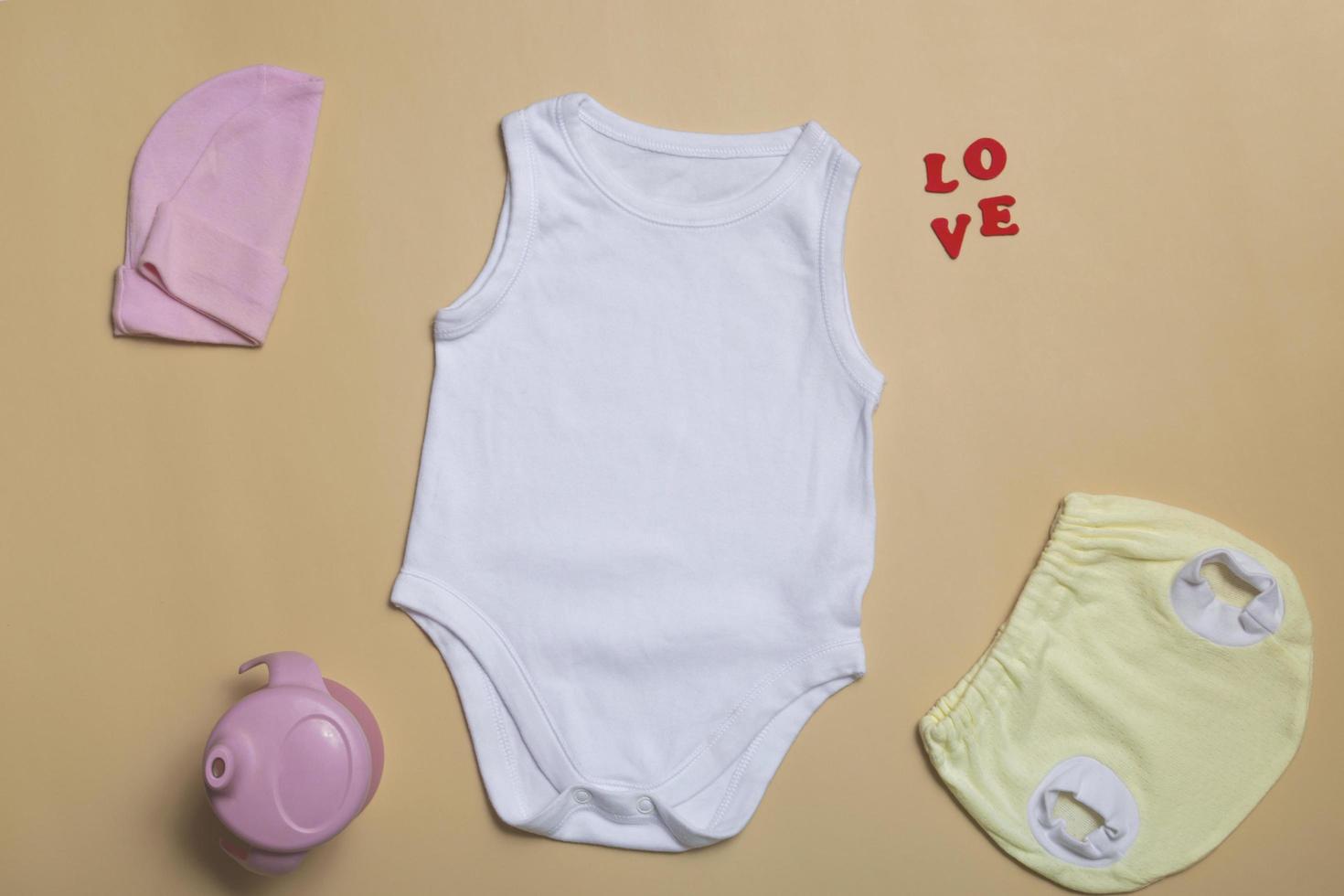 vista dall'alto ravvicinata. mockup di body bianco vuoto, mutandine neonate gialle su sfondo beige, con spazio per la copia - modello di mockup di vestiti per bambini perfetti foto