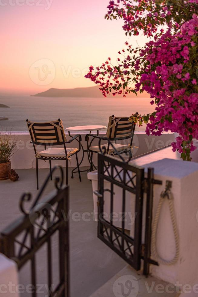 bella vista della caldera e godersi uno scenario romantico tramonto sul mar egeo, santorini. vacanza di viaggio di coppia, destinazione per la luna di miele. romanticismo con fiori, tavolo due sedie e vista mare. vacanza di lusso foto