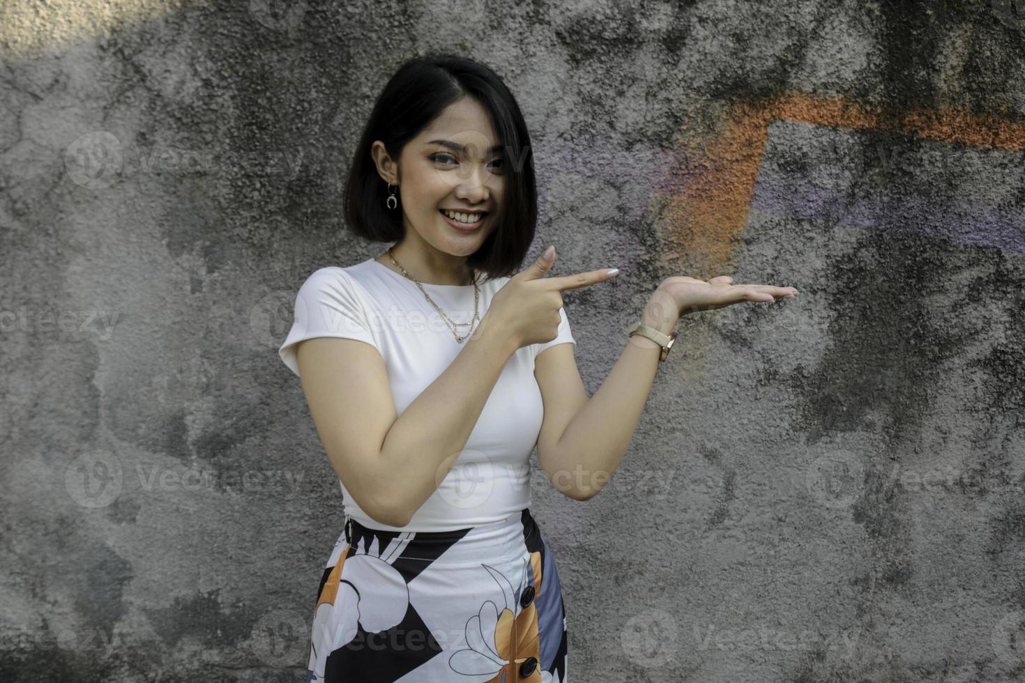 faccia felice e sorridente con il sorriso di una giovane ragazza asiatica con il punto della mano sullo spazio vuoto. foto