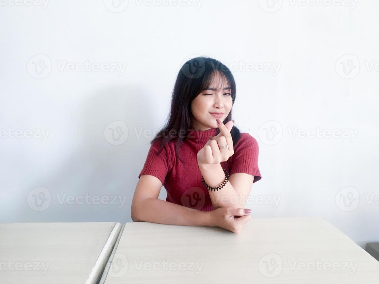 asiatico bella ragazza sorridente che mostra amore corea segno con il dito con sfondo sfocato isolato sfondo bianco. donne indonesiane foto