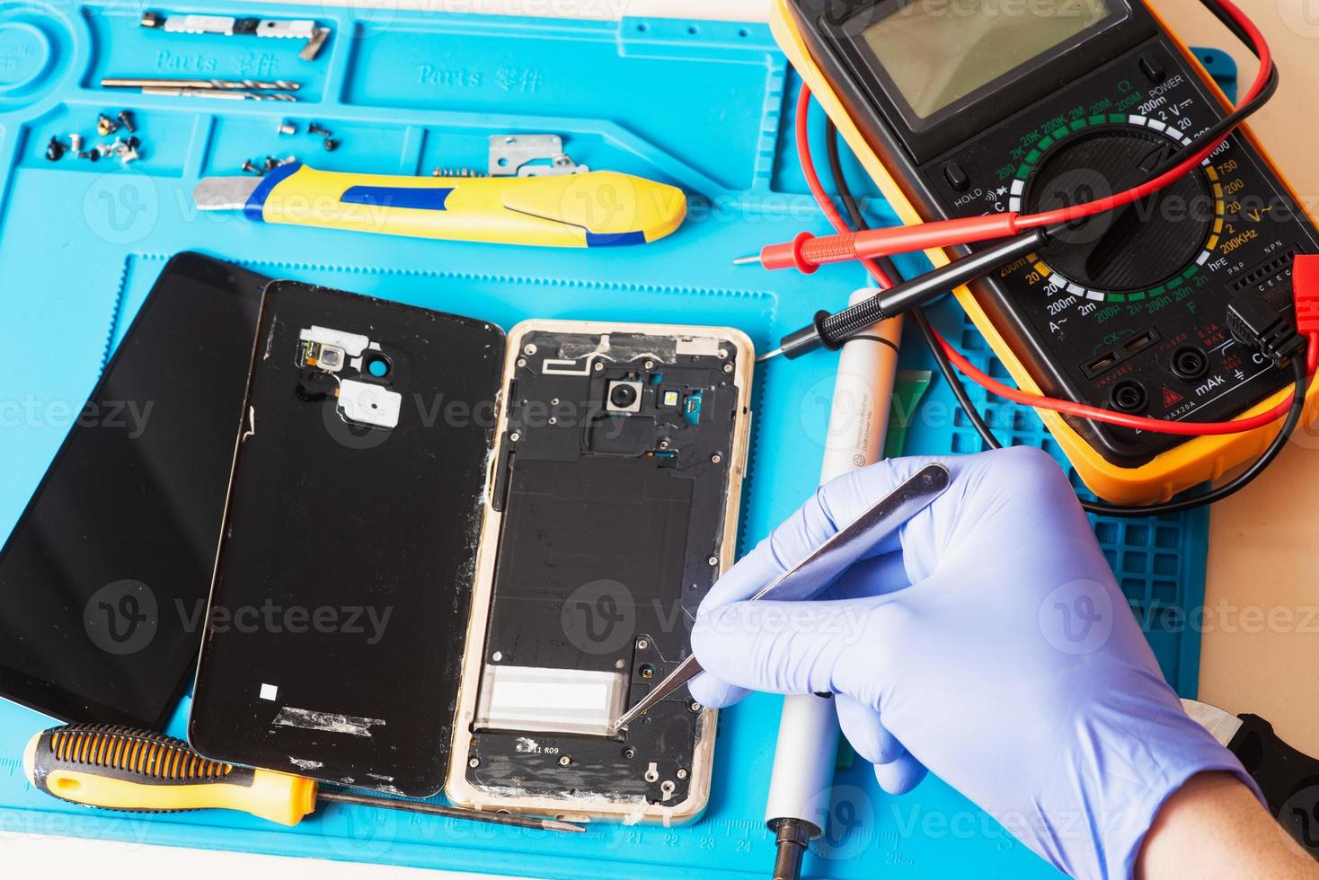 artigiano in guanti di gomma ripara o ripara un telefono cellulare su uno speciale tappetino in gomma per la riparazione. vista dall'interno foto