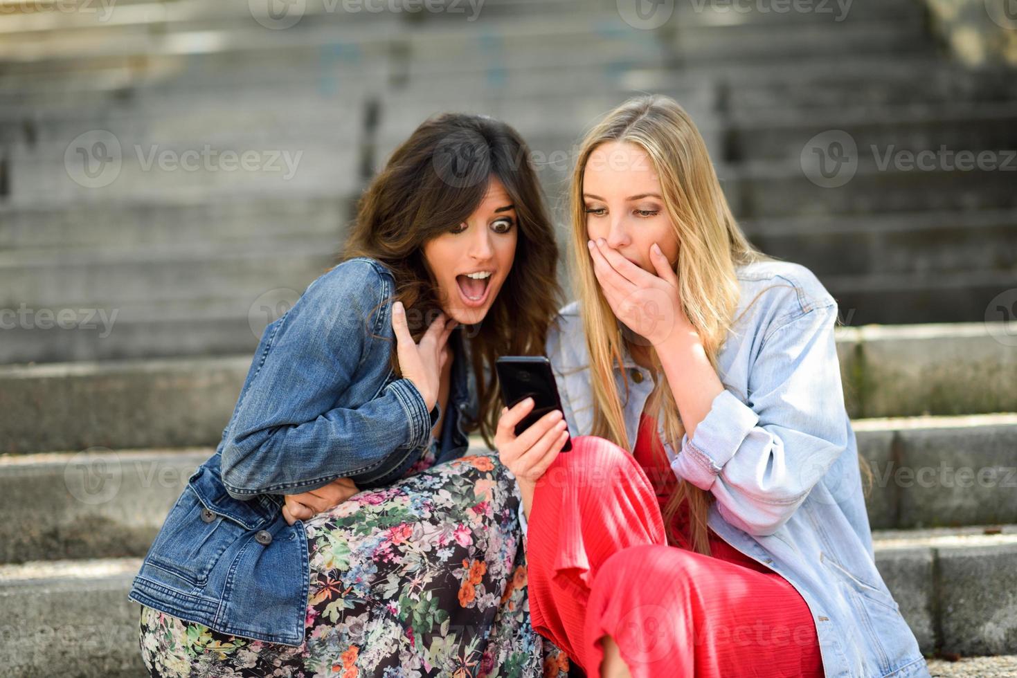 due donne stupite da ciò che vedono sul loro smartphone foto