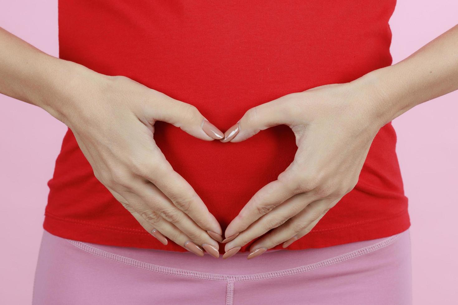 mani di una madre che indossa la pancia nel segno del cuore o nel simbolo. concetto di amore, cura e donna in attesa della venuta del neonato. primo piano foto