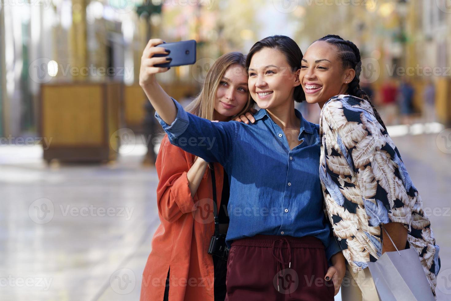 donne multirazziali sorridenti che prendono selfie in città foto