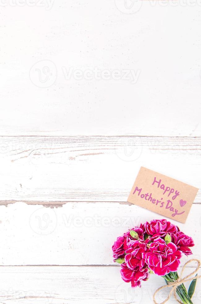 Fotografia concettuale per la festa della mamma - bellissimi garofani con carta modello isolata su un tavolo di legno luminoso, spazio per la copia, distesi, vista dall'alto, mock up foto