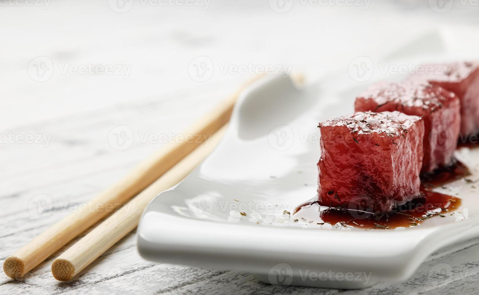 sashimi di tonno immerso in salsa di soia, sale denso e aneto su una vecchia tavola di legno bianca con le bacchette. pesce crudo in stile tradizionale giapponese. immagine orizzontale. foto