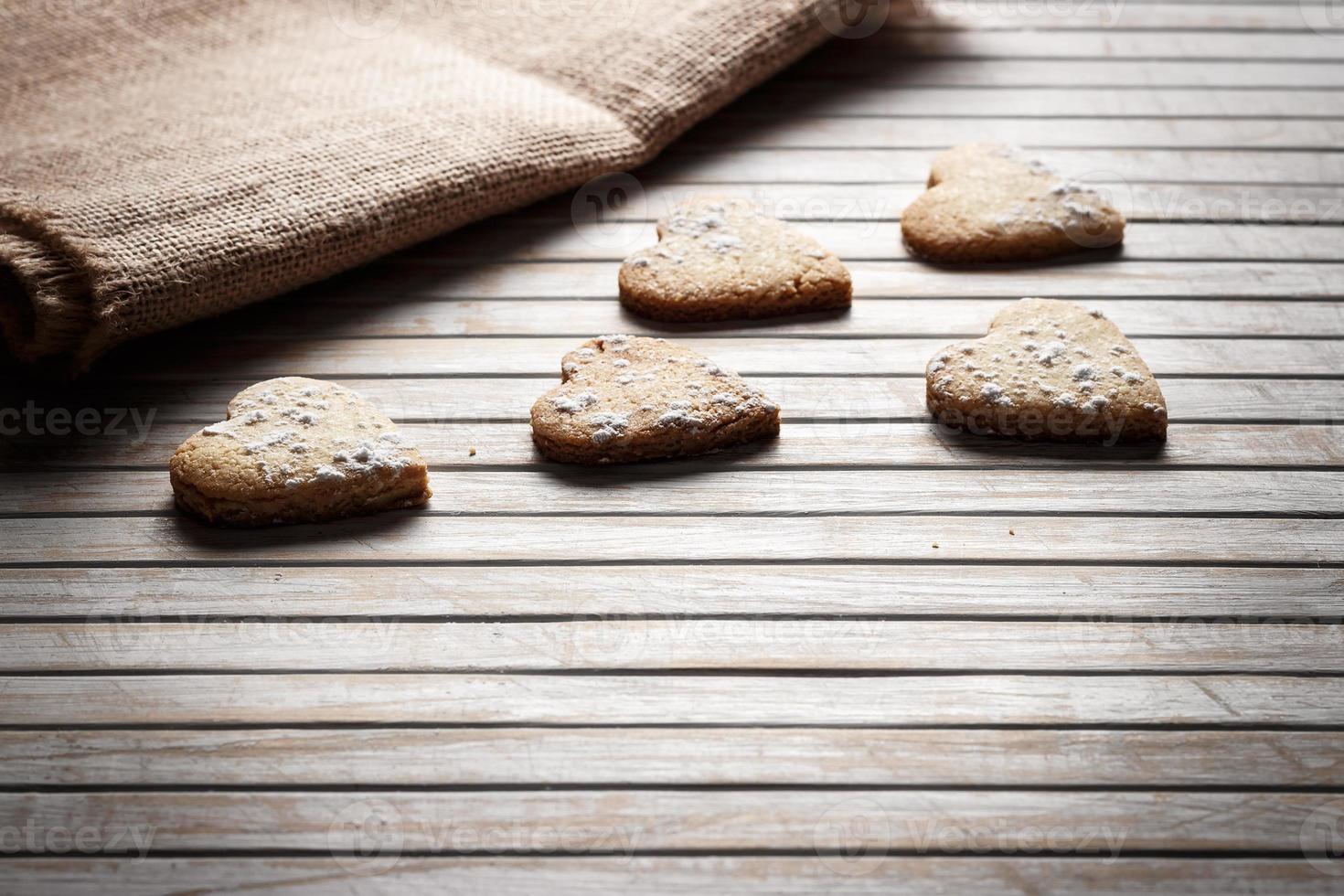 deliziosi biscotti fatti in casa a forma di cuore cosparsi di zucchero a velo su una tavola di legno con tela di sacco sullo sfondo. immagine orizzontale vista in controluce. foto