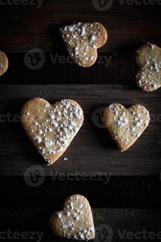 deliziosi biscotti fatti in casa a forma di cuore cosparsi di zucchero a velo su una tavola di legno. immagine verticale vista dall'alto. stile lunatico scuro. foto