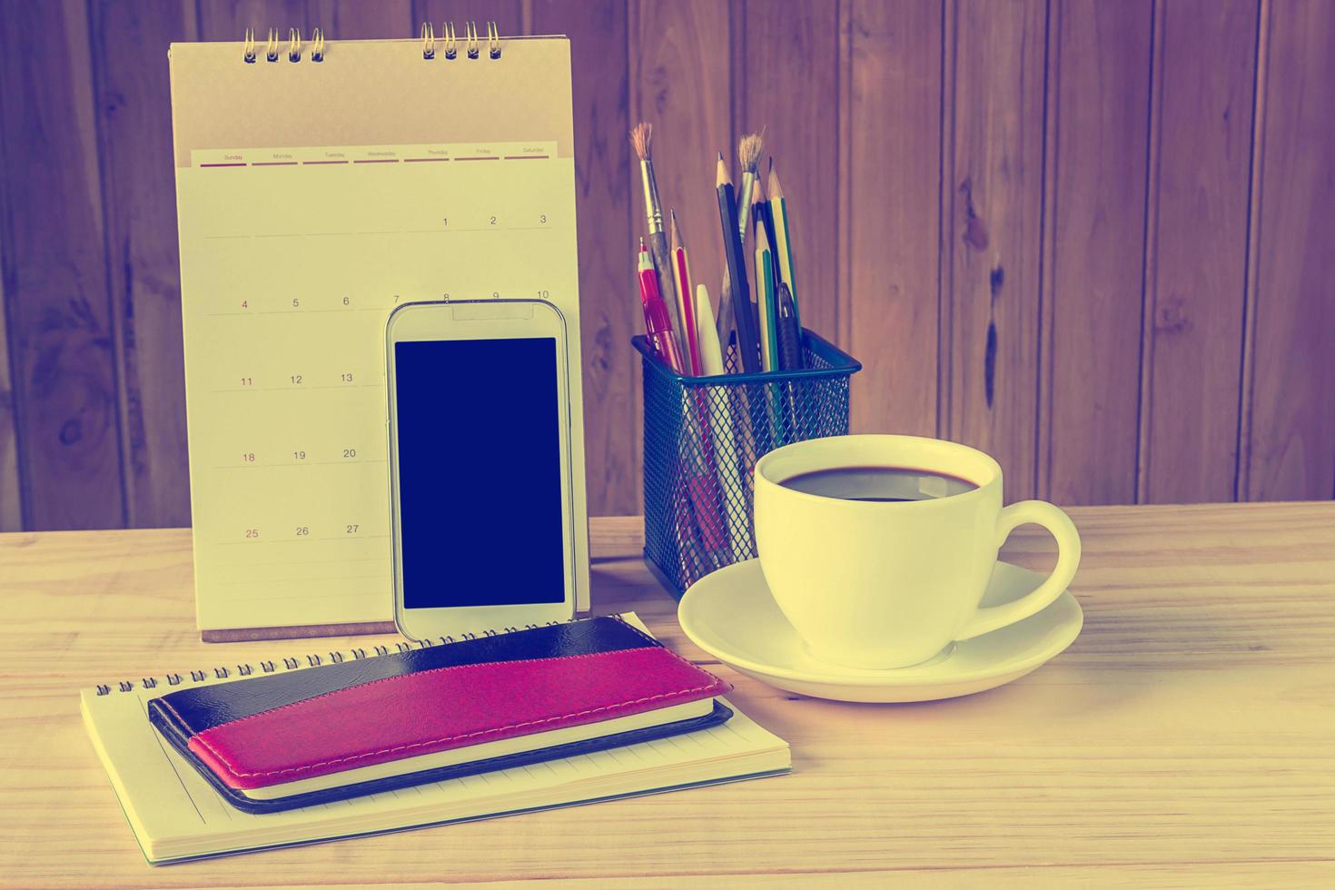 taccuino, smartphone, tazza di caffè e pila di libro con calendario sul tavolo di legno foto