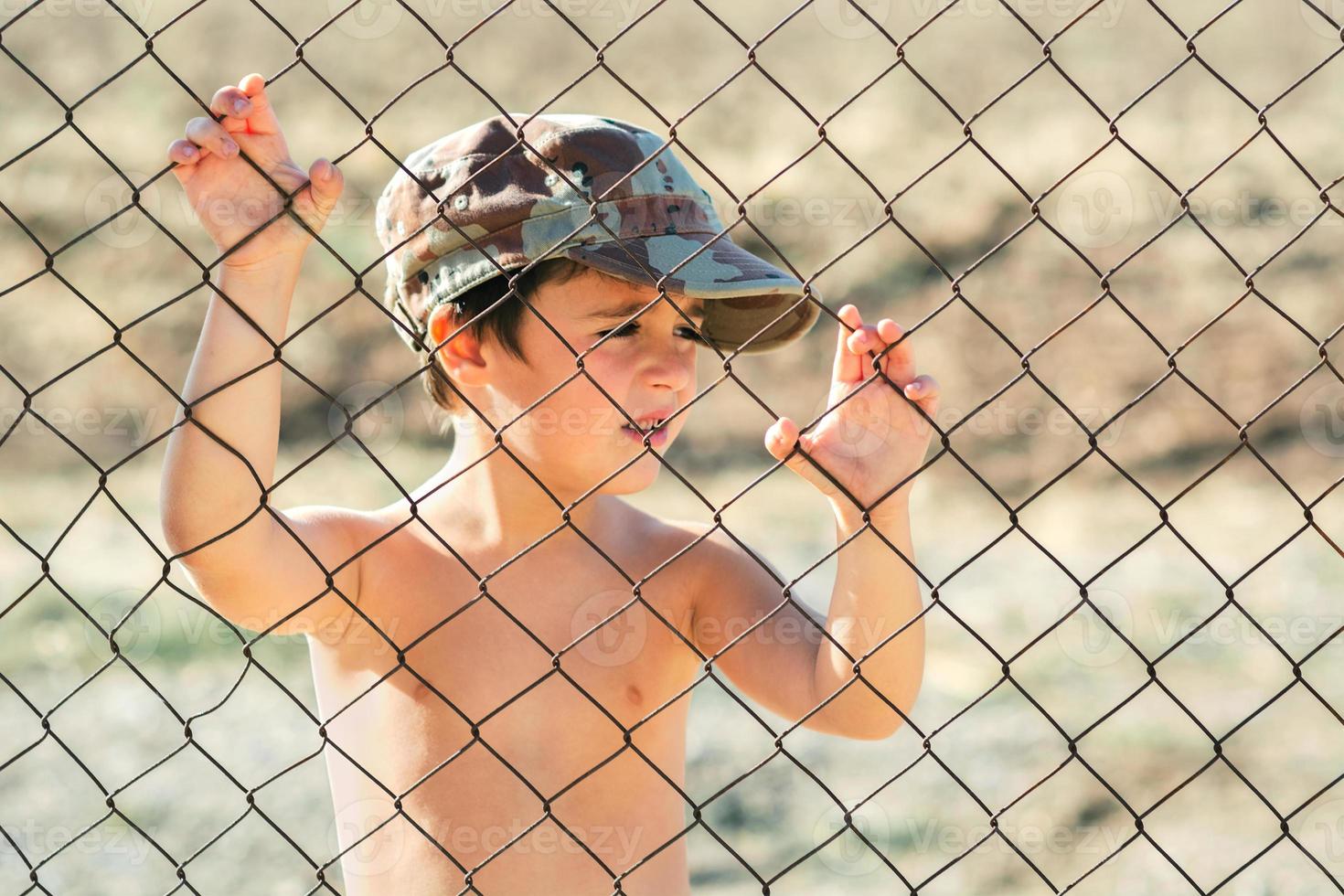 bambino triste con un berretto militare dietro un recinto. fermare il concetto di guerra foto