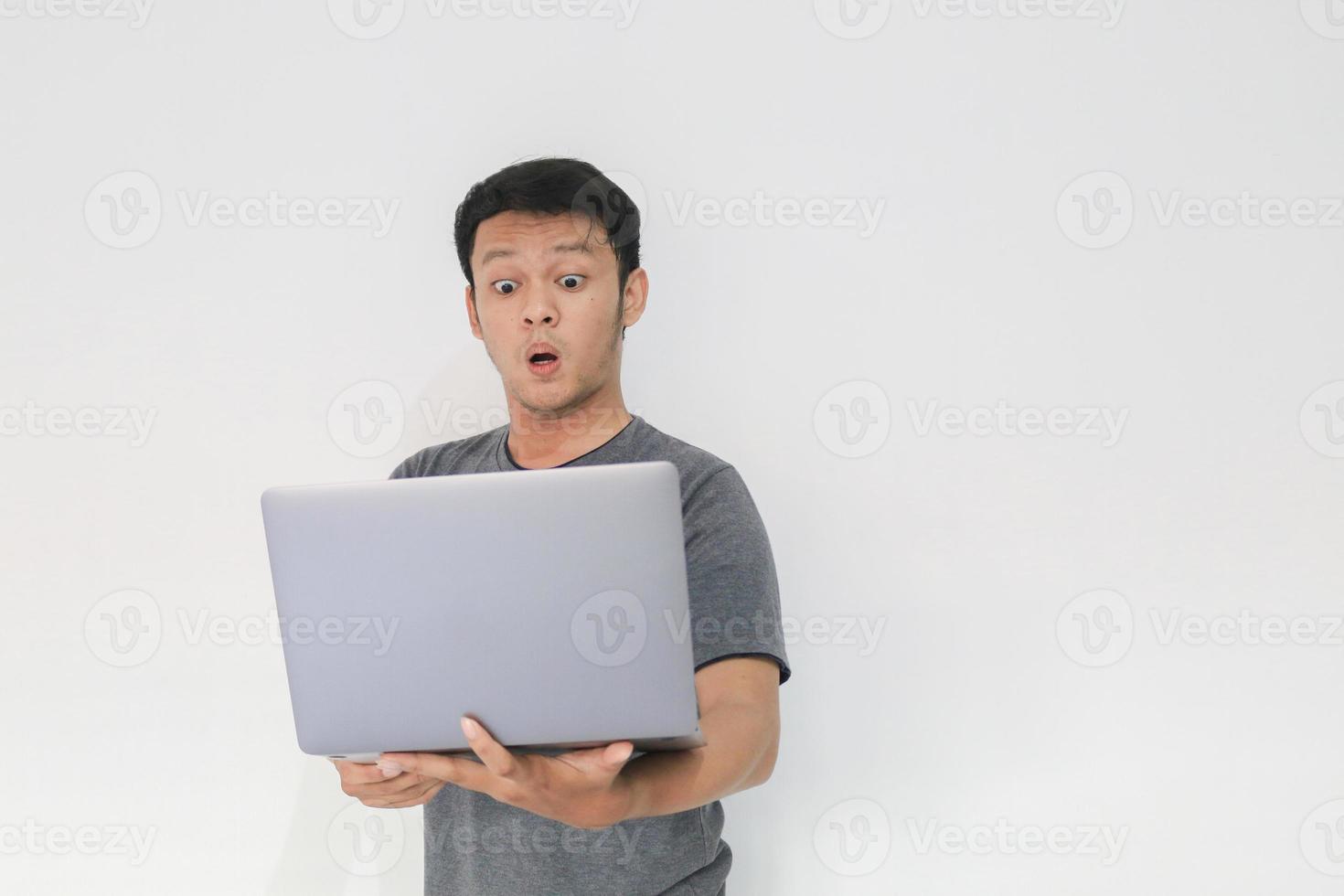 wow il viso del tuo uomo asiatico ha scioccato ciò che vede nel laptop su uno sfondo grigio isolato. foto