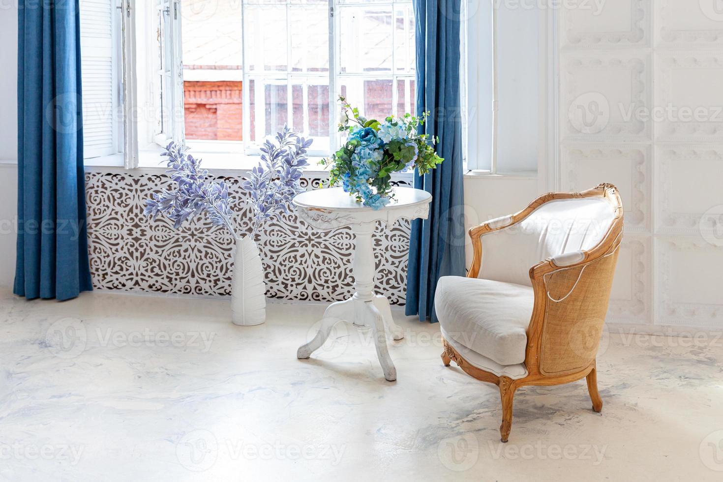 bella camera da letto interna pulita bianca luminosa classica di lusso in stile barocco con ampia finestra, poltrona e composizione floreale. foto