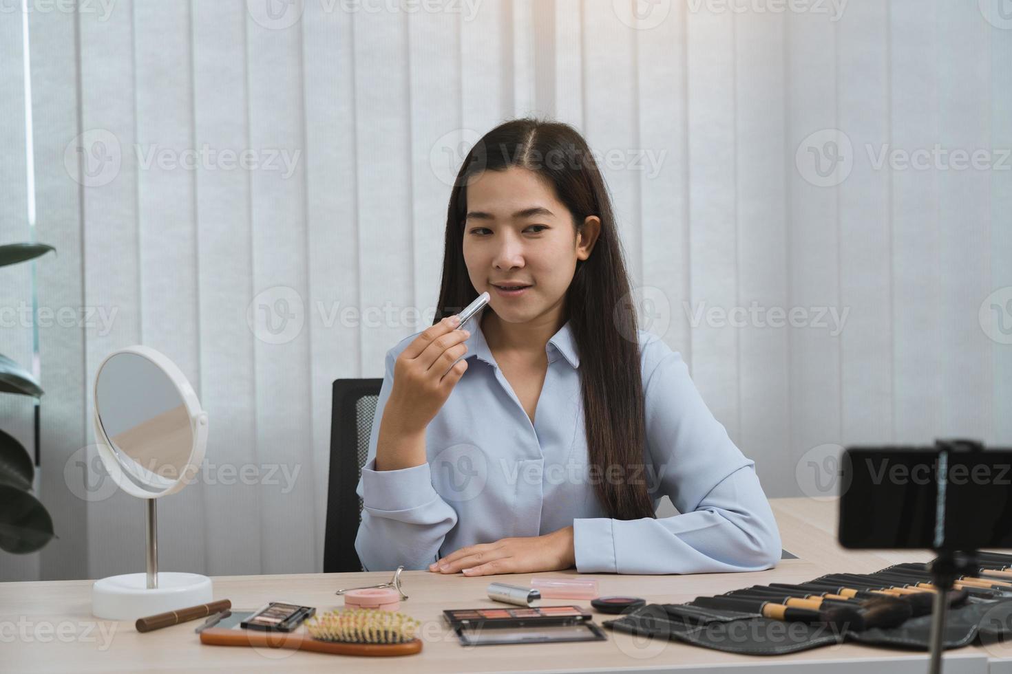 giovane donna asiatica che registra se stessa sui prodotti di bellezza realizzando un video per il suo blog sui cosmetici usando la fotocamera del telefono a casa. foto