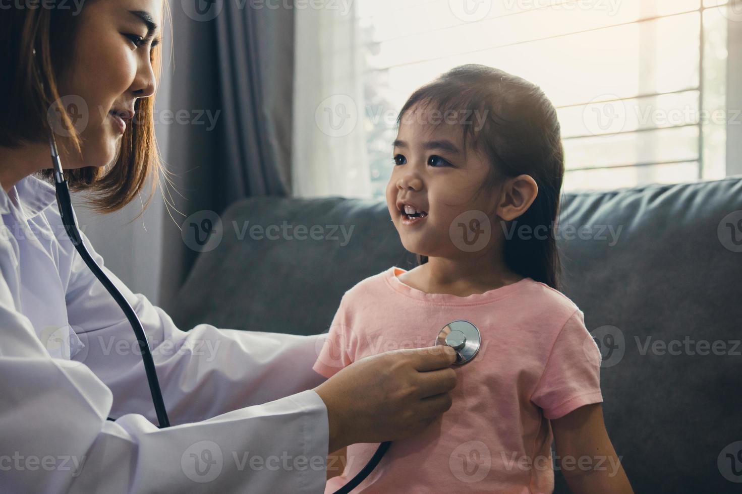 fiduciosa donna asiatica professionista sanitario visita il suo paziente utilizzando uno stetoscopio durante una giovane paziente femminile ben controlla a casa. foto