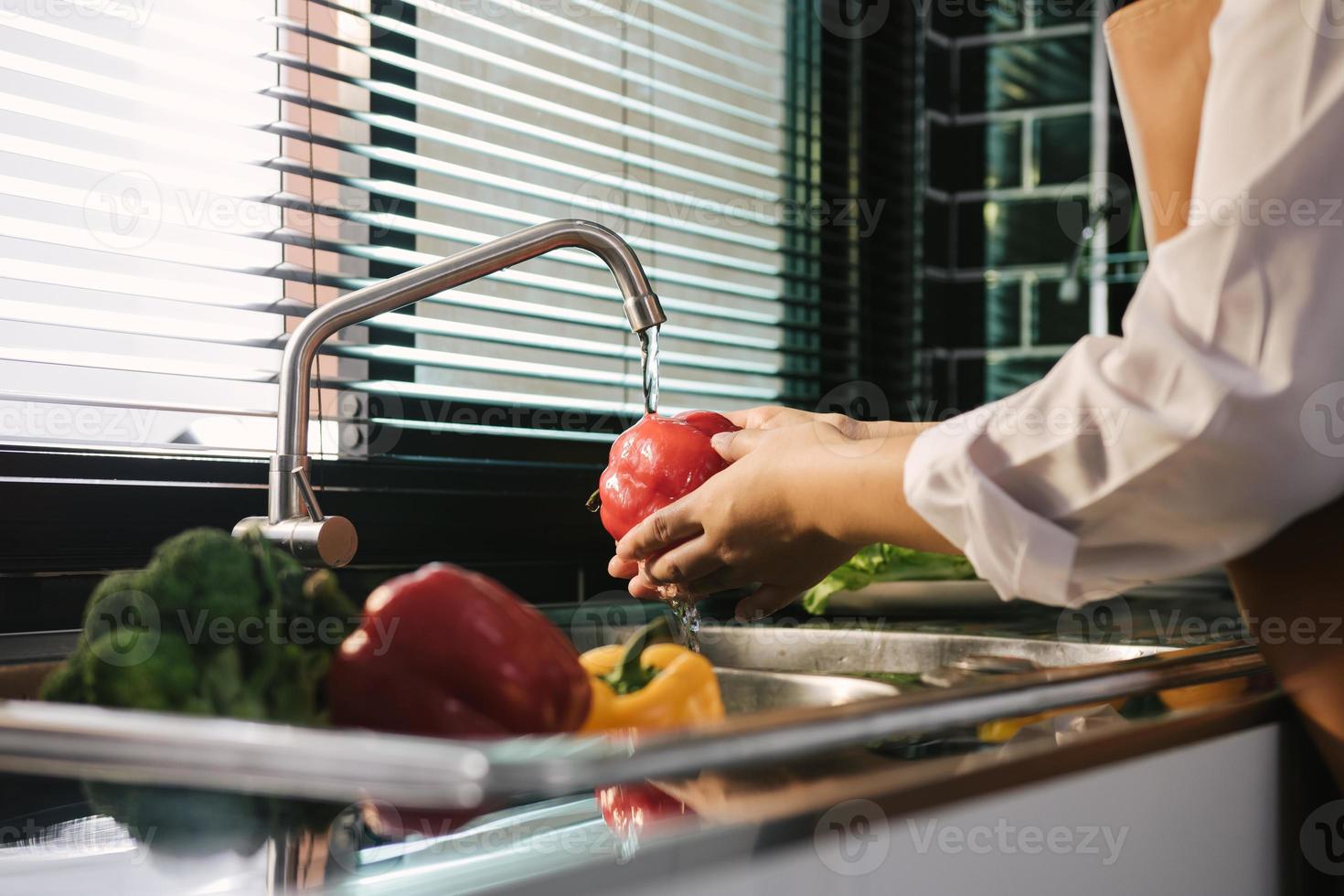 mani asiatiche donna lavaggio verdure peperone e preparazione cibo sano in cucina. foto