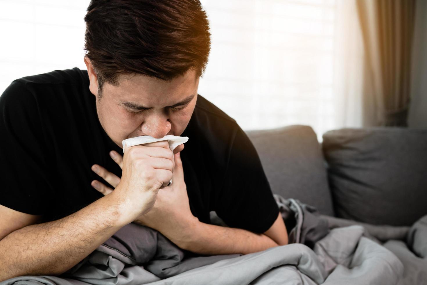 le persone asiatiche sono malate o ammalate di bronchite mentre tossiscono coprendosi la bocca con della carta velina quando si siedono sul divano di casa. foto