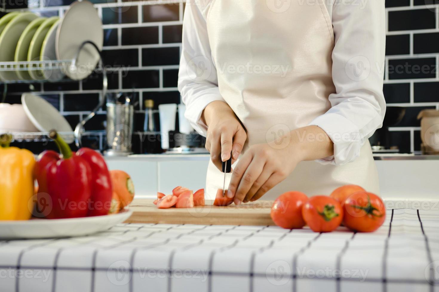 casalinga con coltello e mani che tagliano il pomodoro su tavola di legno nella stanza della cucina. foto