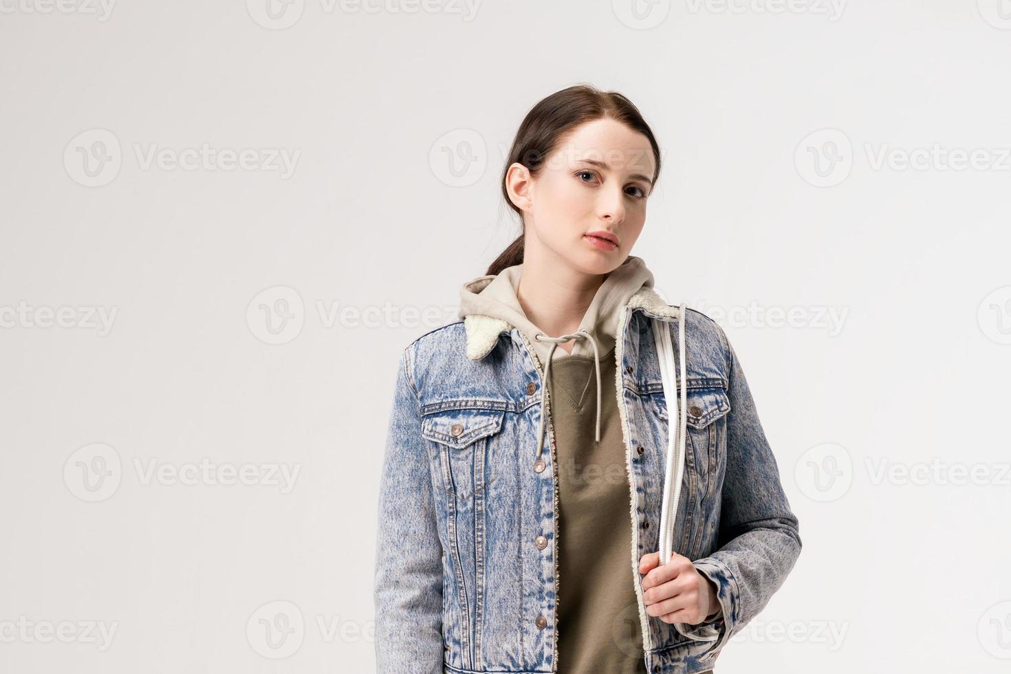 giovane donna carina in una giacca di jeans e con uno zaino in posa su uno sfondo bianco foto