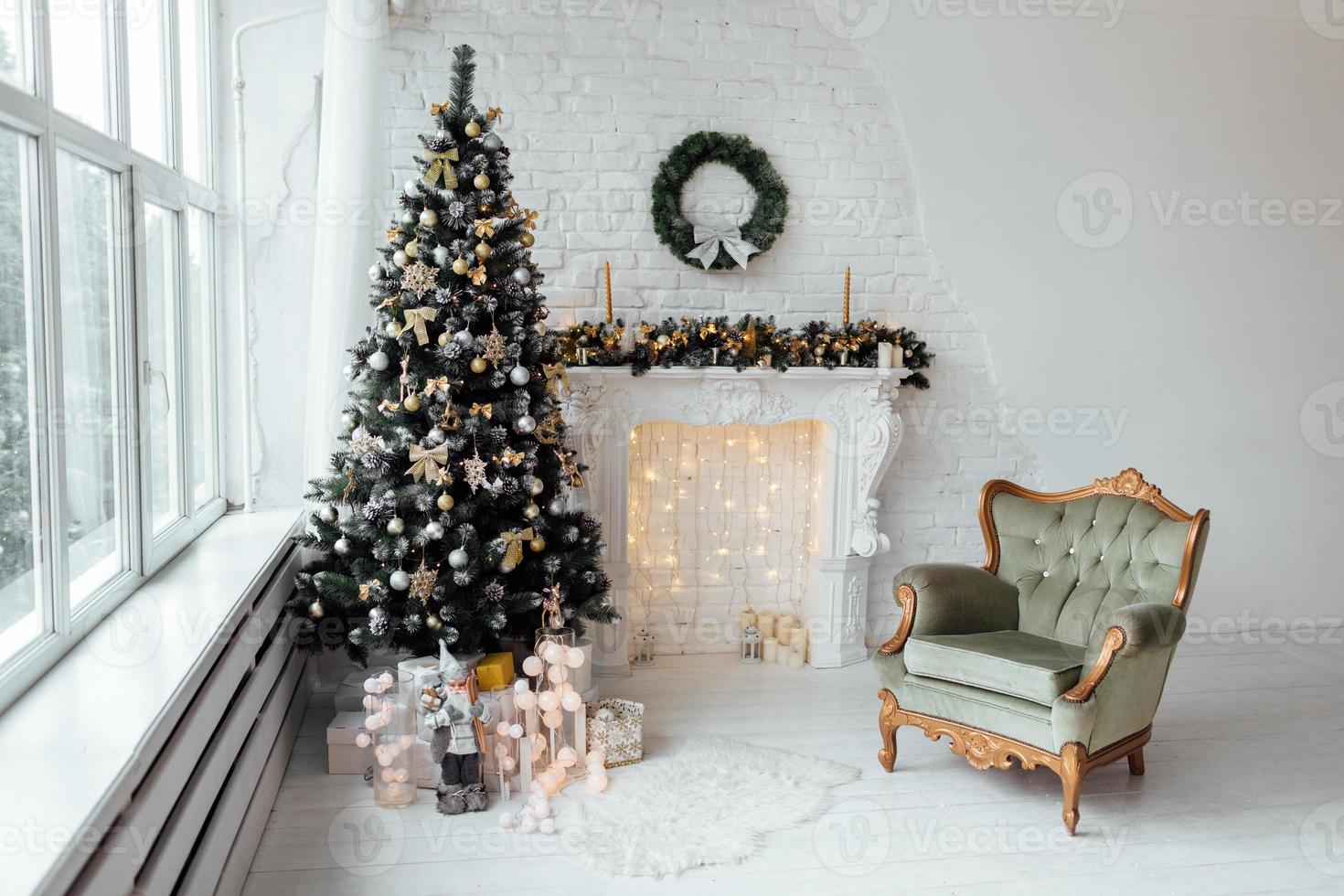 bella camera decorata per le vacanze con albero di natale con scatole regalo sotto di esso in bianco e blu. ampia vetrata panoramica, camino e poltrona in stile classico foto