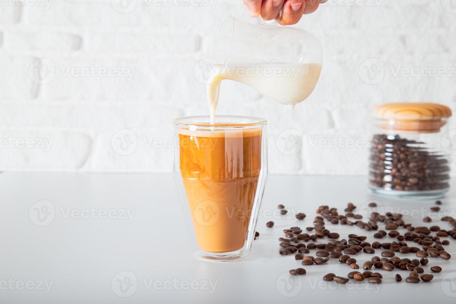 una mano anonima sta versando il latte in un bicchiere di caffè a doppia faccia. foto