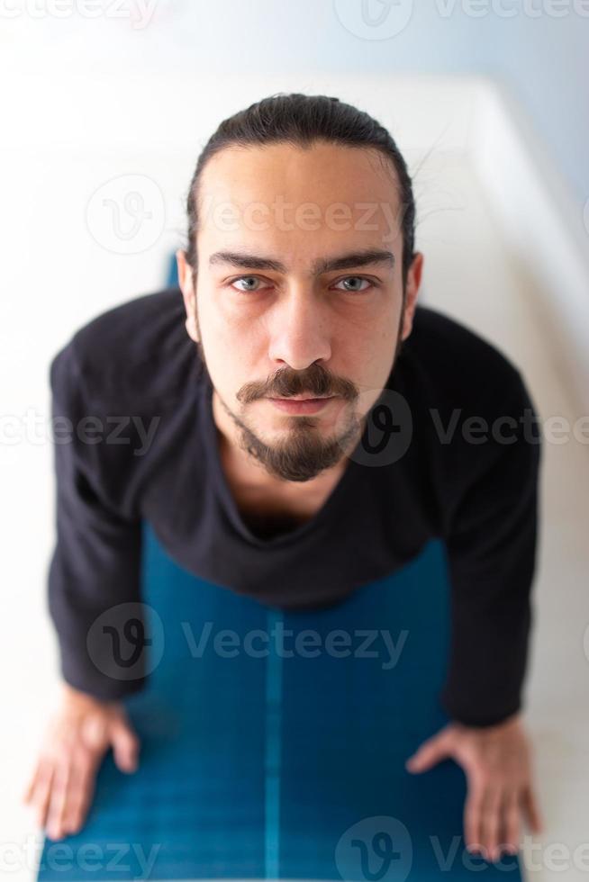 giovane uomo bianco dai capelli lunghi caucasico sta eseguendo yoga in uno studio o in una casa. foto