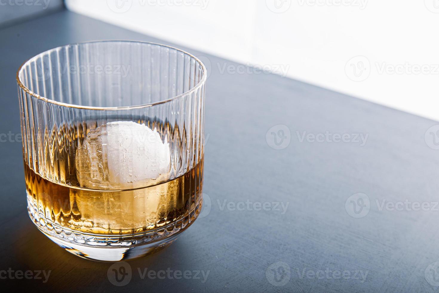 cubetto di ghiaccio a forma di sfera e vista ravvicinata del whisky dallo studio. foto
