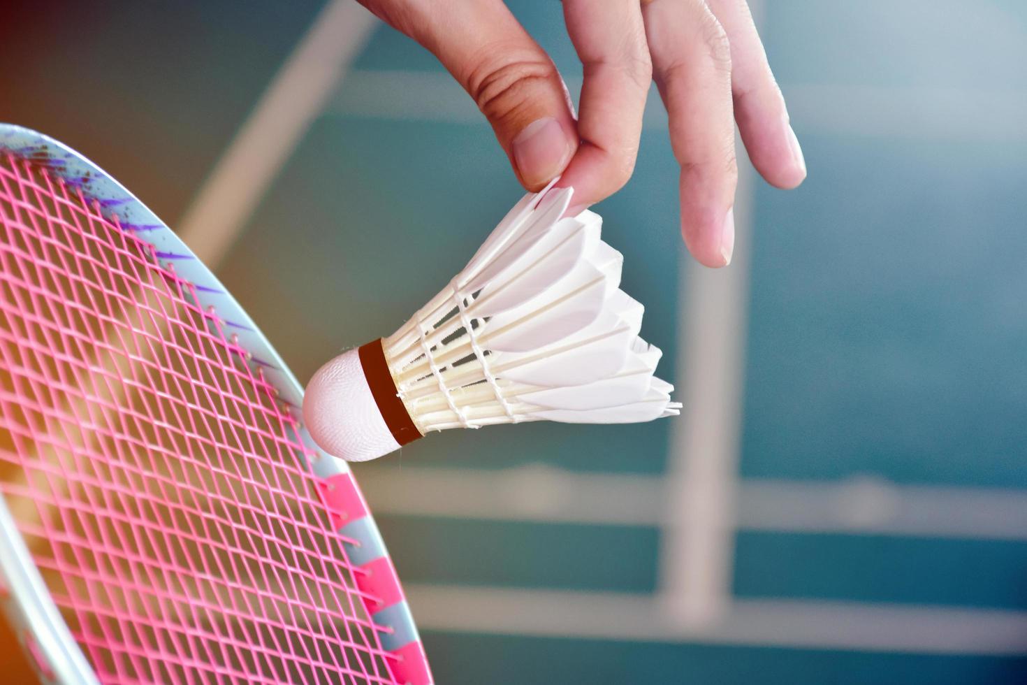 racchetta da badminton e vecchio volano bianco che tiene nelle mani del giocatore mentre lo serve sulla rete davanti, sfocatura dello sfondo del campo da badminton e messa a fuoco selettiva. foto