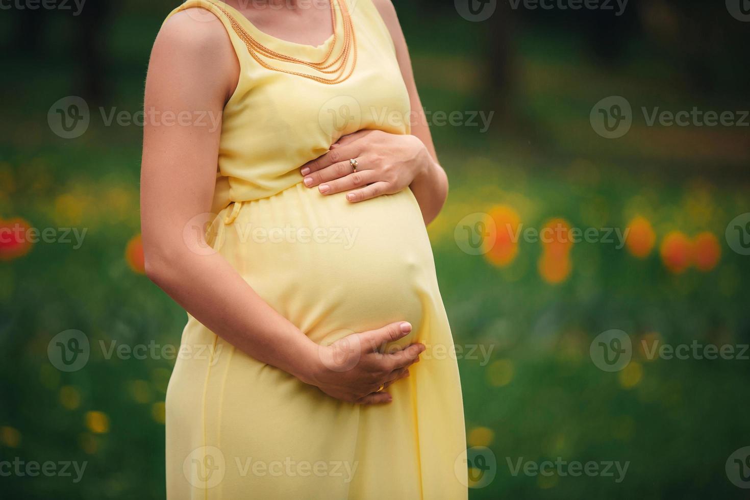ragazza incinta in un vestito giallo che abbraccia il suo stomaco nel campo foto
