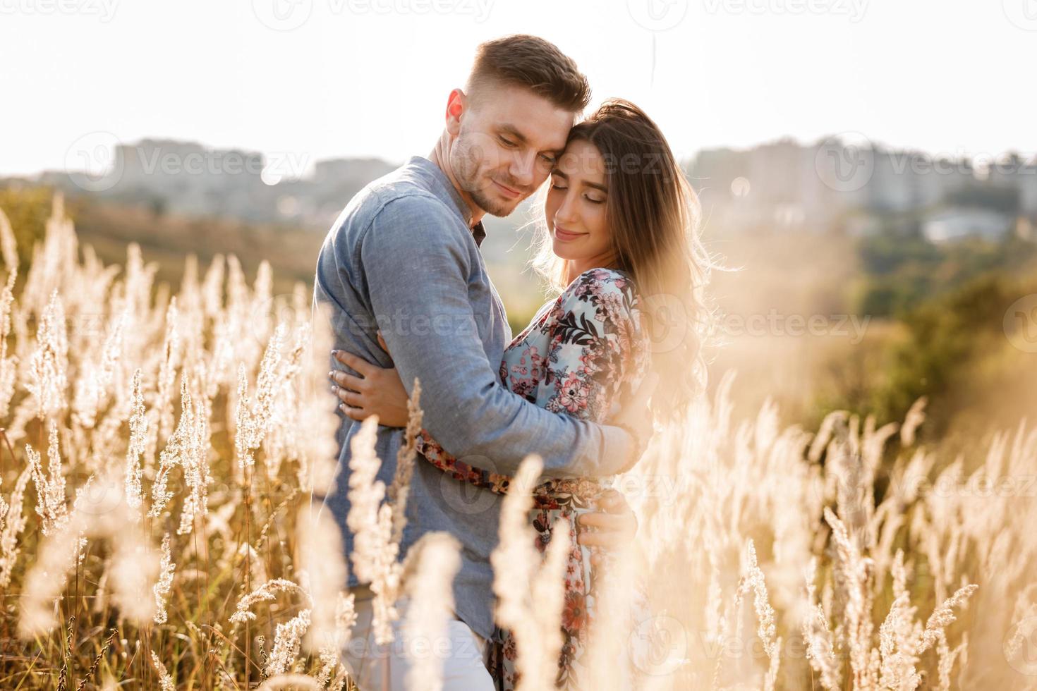bella giovane coppia che si abbraccia in un campo con erba al tramonto. uomo e donna alla moda che si divertono all'aperto. concetto di famiglia. copia spazio. foto