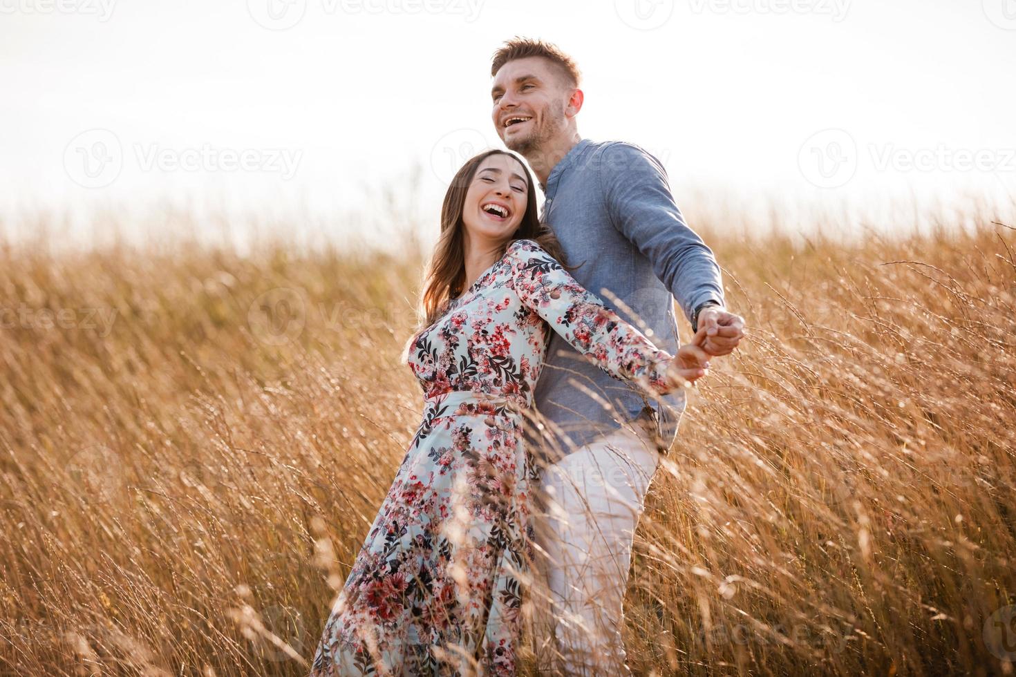 bella giovane coppia che si abbraccia in un campo con erba al tramonto. uomo e donna alla moda che si divertono all'aperto. concetto di famiglia. copia spazio. foto