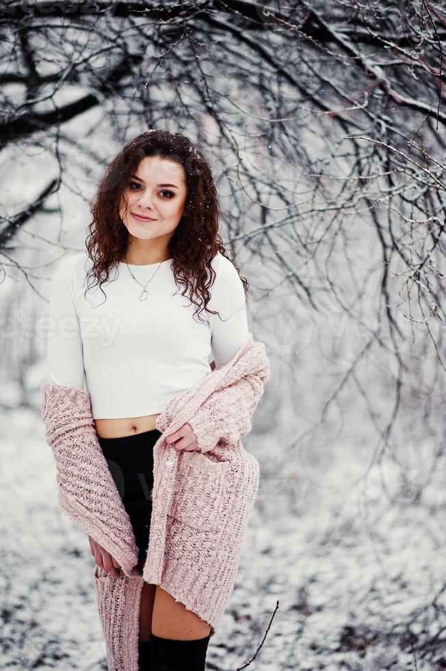 sfondo ragazza bruna riccia neve che cade, indossare un maglione caldo lavorato a maglia, minigonna nera e calze di lana. modello in inverno. ritratto di moda con tempo nevoso. foto dai toni di instagram.